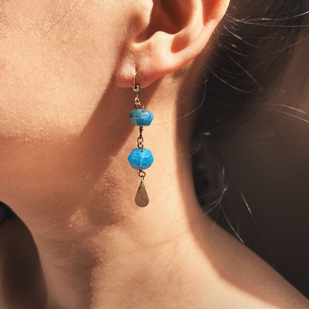 The Yoga Retreat in Bali Earrings is handcrafted from the 14K Gold-filled wire hook, natural peacock blue faceted Apatite bead with dazzling brass charms.